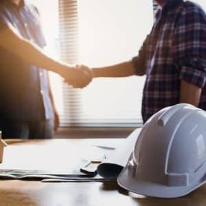Hard hat on table and two people shaking hands
